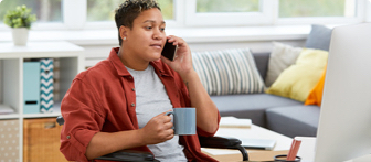 A person using a wheelchair talking on the phone and holding a cup of coffee.